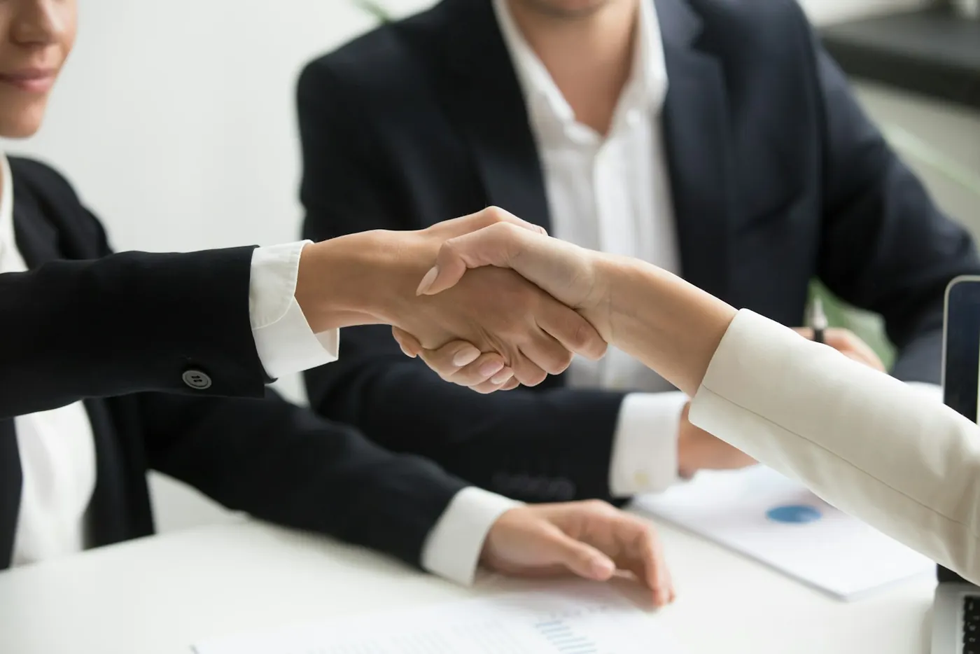 Two people shaking hands over a laptop