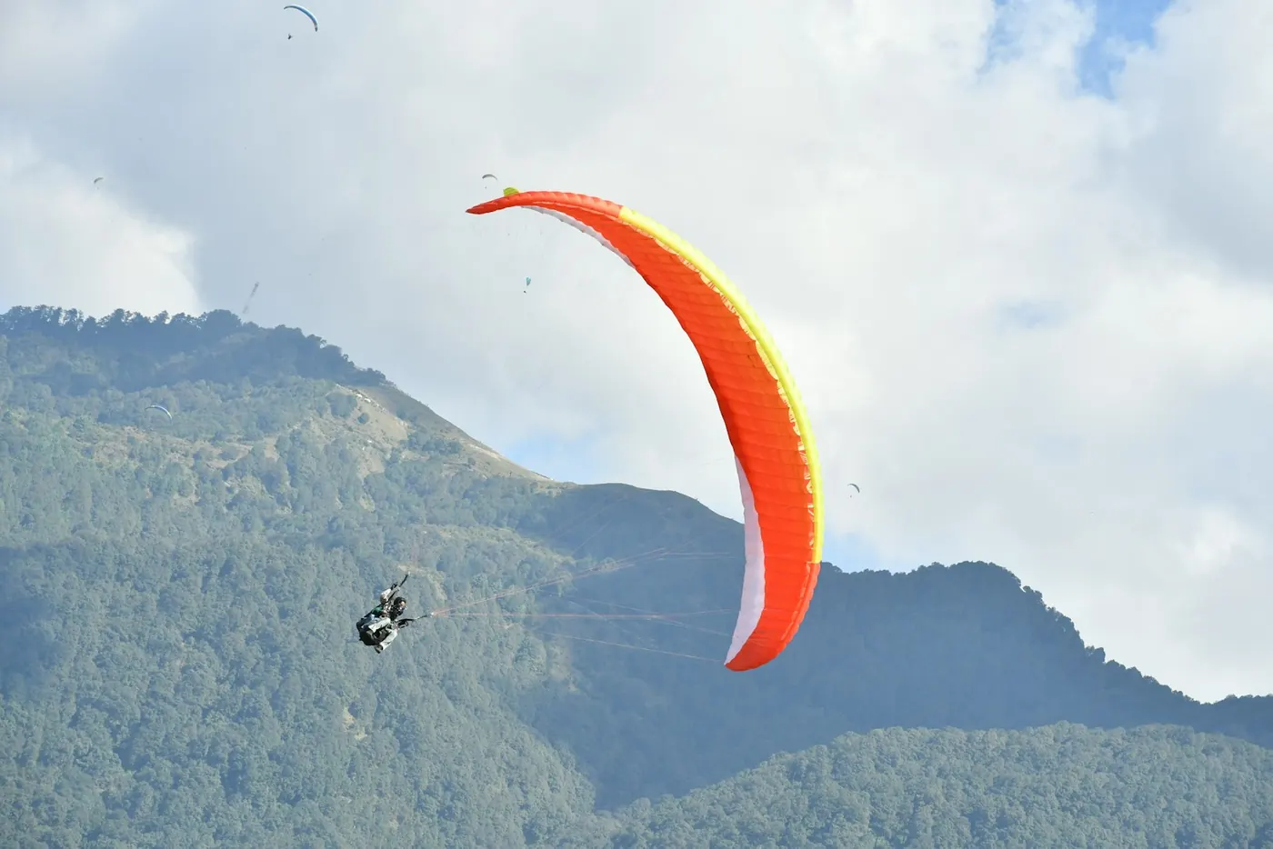 An orange paraglider above green mountains
