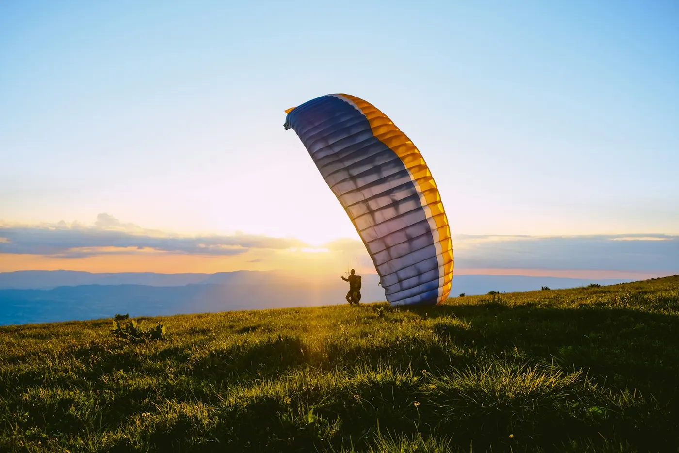 A paraglider standing on a hilltop at sunset